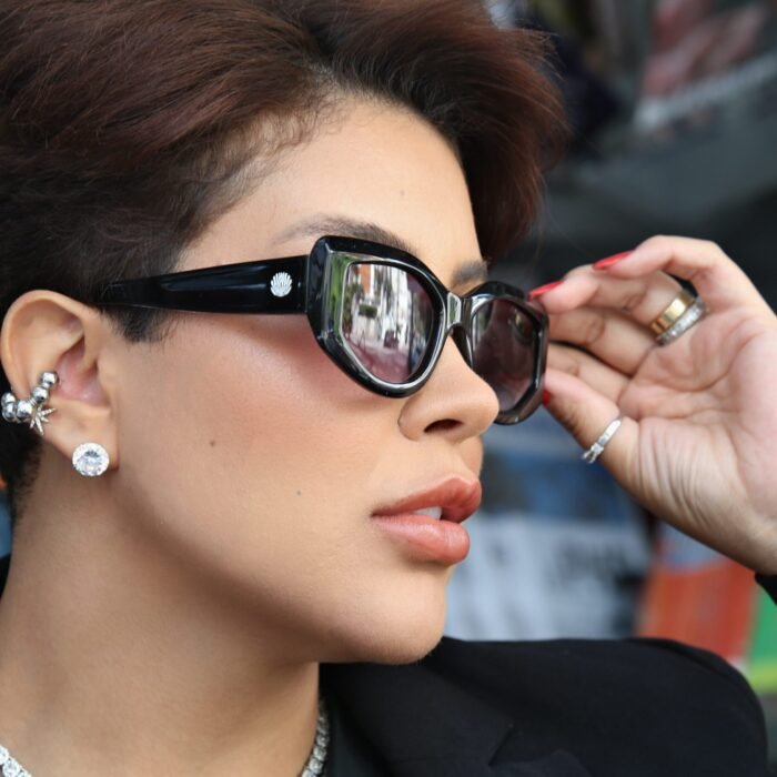 Close lateral de uma mulher usando óculos de sol Black Bat Flower da Use Let’s, com armação preta e lentes escuras, segurando levemente a haste do óculos