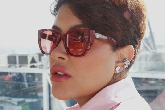 Mulher estilosa usando óculos de sol vermelho modelo Hooker’s Lips da Use Let’s Brasil, com armação em acetato e lentes degradê, posando em ambiente urbano com fundo desfocado de prédios